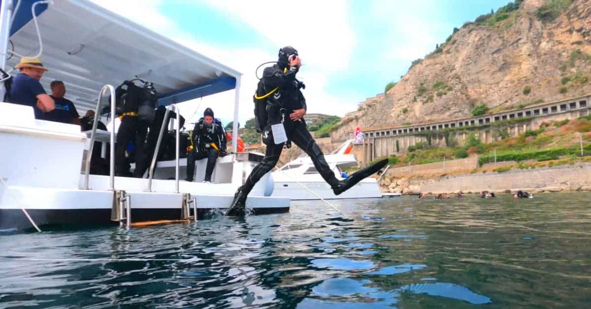 Scuba diver che si immerge dall'imbarcazione in acque cristalline.