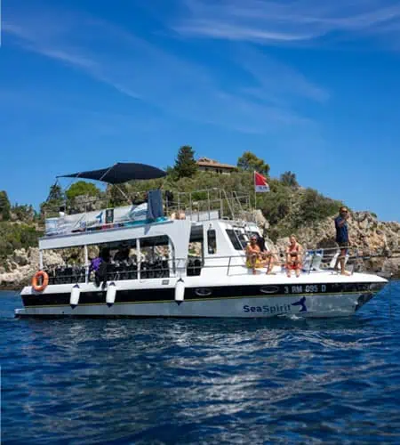 Barca Sea Spirit in mare con turisti che si godono il sole e il paesaggio costiero.
