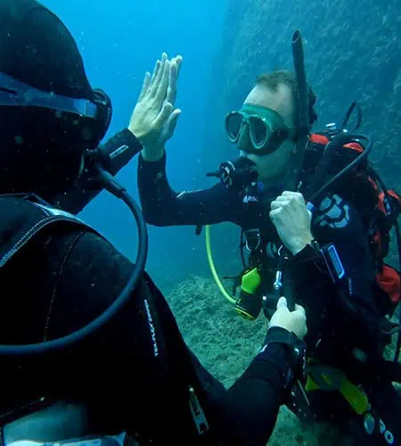 Due subacquei si salutano sott'acqua con attrezzature da immersione.