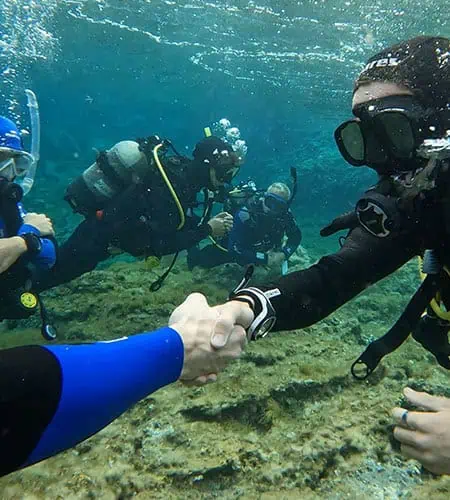 Immagine di subacquei che si stringono la mano sott'acqua, simbolo di amicizia e avventura marina.