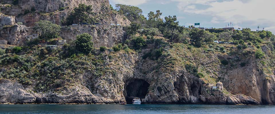 Scogliera con grotta marina e barca vicino alla costa di La Grotta del Giorno.