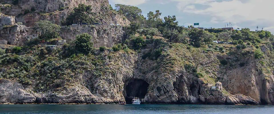 Scogliera con grotta marina e barca vicino alla costa di La Grotta del Giorno.