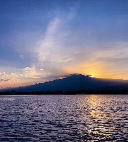 Tramonto sul mare con montagna e cielo colorato al tramonto.