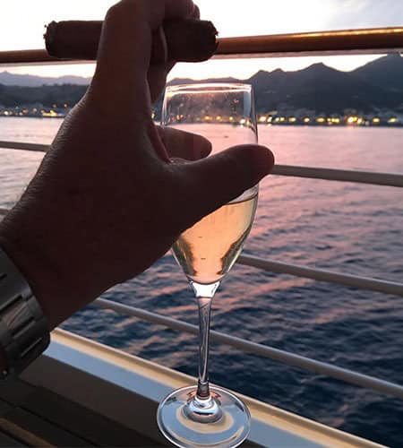 Bicchiere di champagne in mano con vista mare al tramonto.