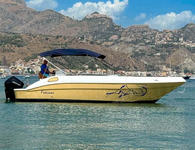 Barca a motore con nome "Fabiane" naviga in acque calme, sfondo montano e cielo sereno.